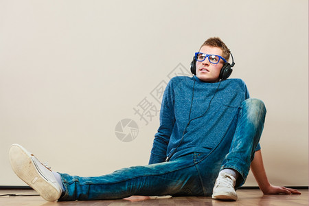 年轻时装男耳机坐在地板上听音乐玻璃杯高清图片素材