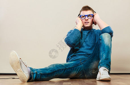 年轻时装男耳机坐在地板上听音乐人高清图片素材