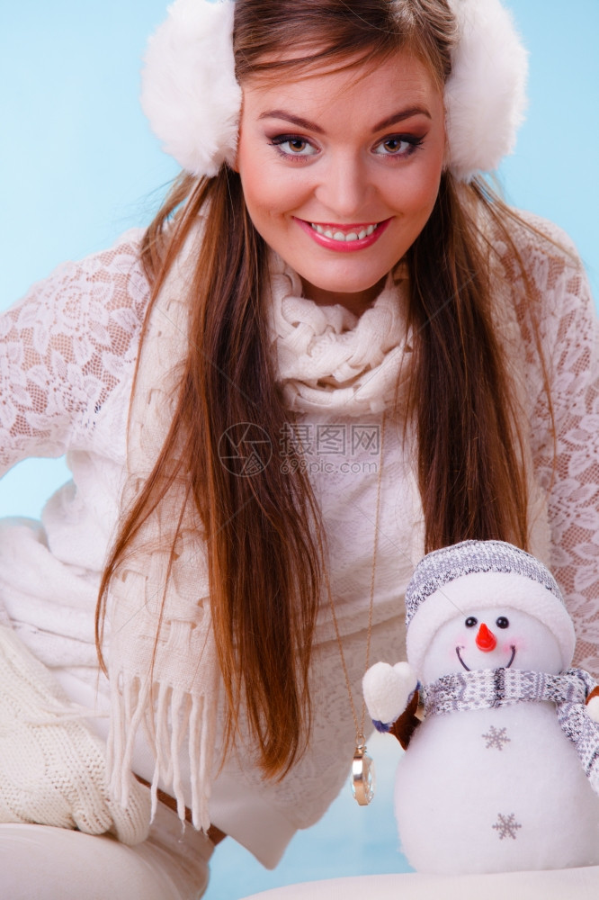 带着小雪人笑的可爱女穿着耳毛和白色衣的迷人女孩穿着蓝色工作室图片