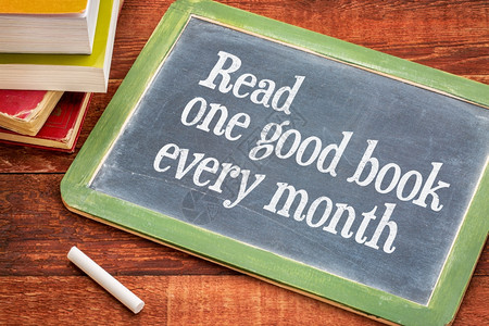每月读一本好书在黑板上提供建议或醒用白粉和一堆书籍用铁制木餐桌对着铁的木餐桌背景图片