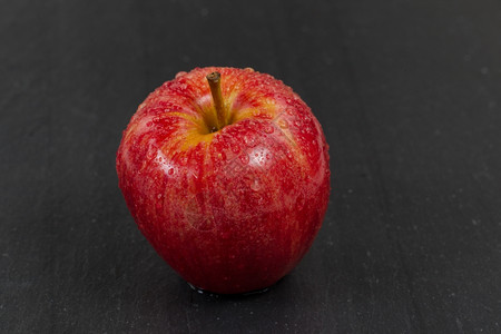 紧贴着一整个红苹果上面覆盖着水滴下面有天然石块选择地聚焦于水果的前部图片