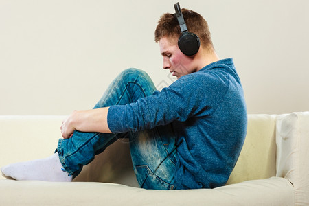 年轻的英俊男子带着耳机坐在沙发上集中地听音乐小伙子高清图片素材