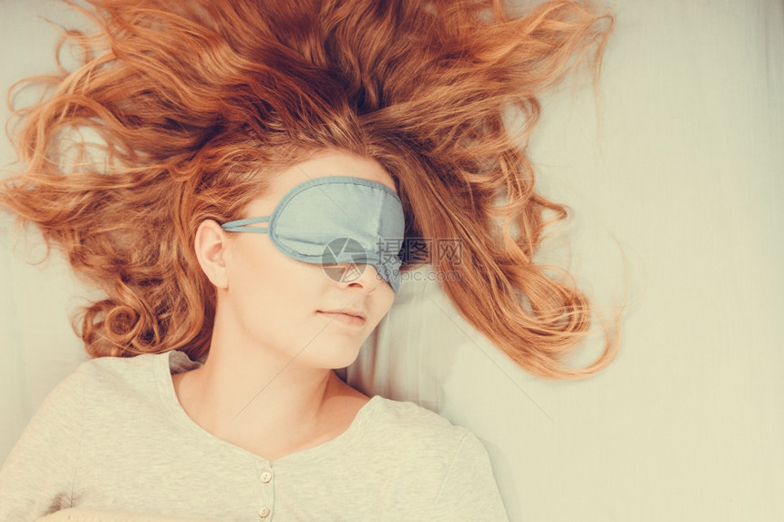 穿着蒙住眼睛的睡梦面具觉妇女穿着蒙住眼睛的睡梦面具在床上的疲劳妇女年轻的孩睡午觉图片