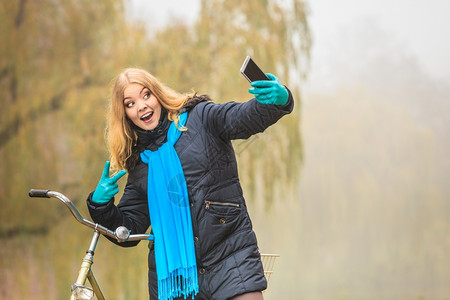 穿着围巾的年轻女孩骑着自行车在公园自拍背景图片
