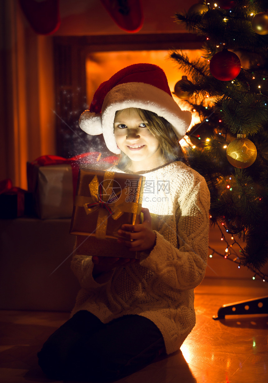 笑的小女孩拿着闪亮的礼物在圣诞树下图片