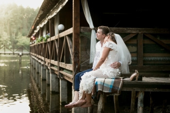 美丽的新娘和郎坐在码头上看着河流和森林图片