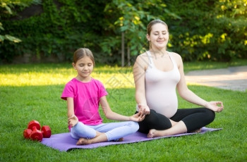 年轻女孩在做瑜伽微笑的孕妇在公园草地上做瑜伽背景