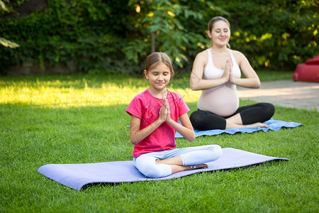 年轻女孩在做瑜伽年轻孕妇和可爱女孩在公园草地上做瑜伽背景