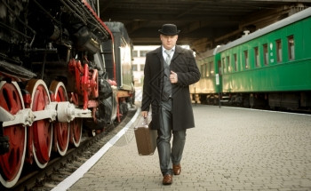 穿旧西装的帅男穿着手提箱在火车平台上行走背景图片