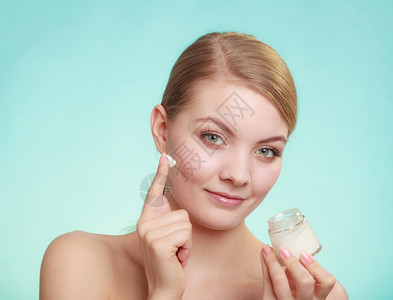 美容治疗女在脸上涂润湿奶油持有皮肤护理产品的罐子绿蓝背景摄影棚拍图片