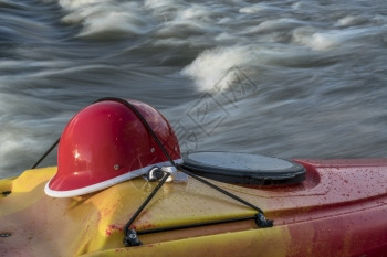 白水皮艇头盔在一条对立快速河流的皮艇甲板上图片