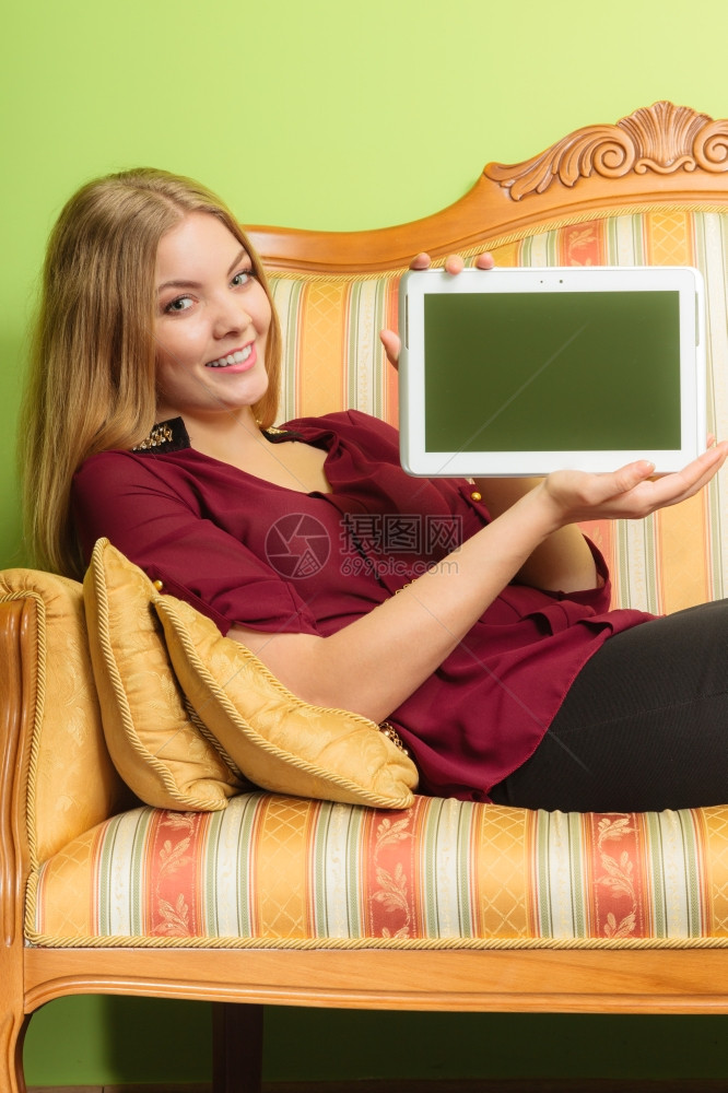 手持平板电脑的笑容优雅女孩手持平板电脑空白屏幕显示复制空间坐在旧沙发上宣传新的现代技术妇女图片
