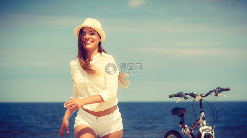 在海滩上骑自行车的女孩运动和娱乐穿着草帽的年轻女孩骑自行车在海滩上休息图片