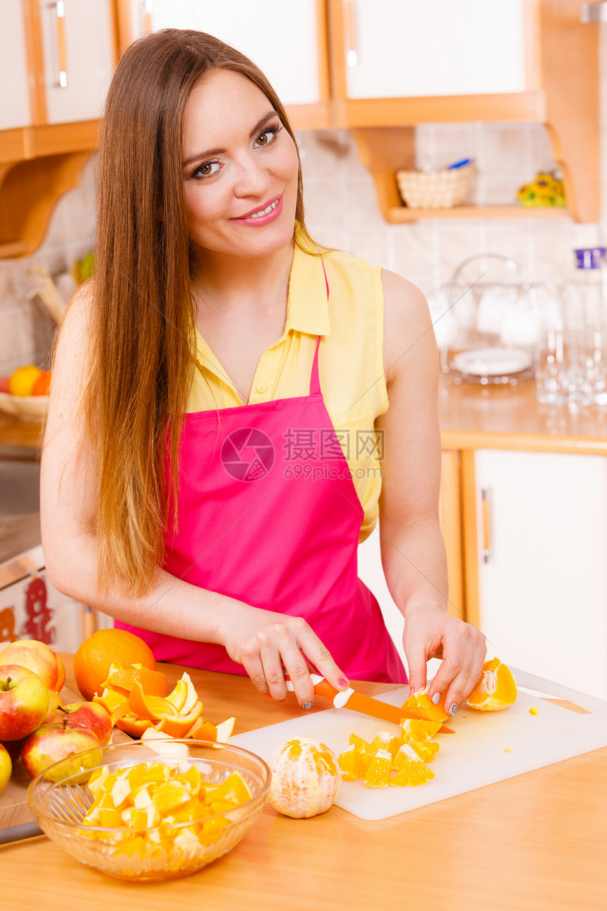 在家厨房的年轻女家庭主妇在切菜板上开新鲜橙子水果用于沙拉或多汁图片