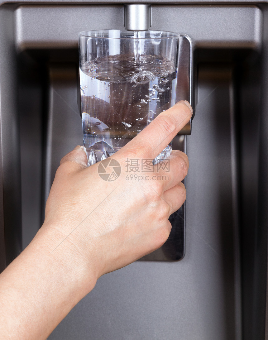 手握着饮用水杯同时冰箱的过滤水填满图片