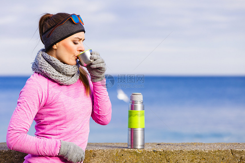 在寒冷的天气中穿着温暖运动服装在户外穿着温暖运动服装的女员适合孩喝着从真空瓶子热水中取出的茶暖和起来图片