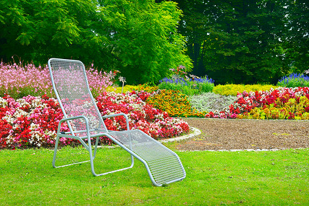 公园躺椅坐在花床旁边的公园甲板椅上背景