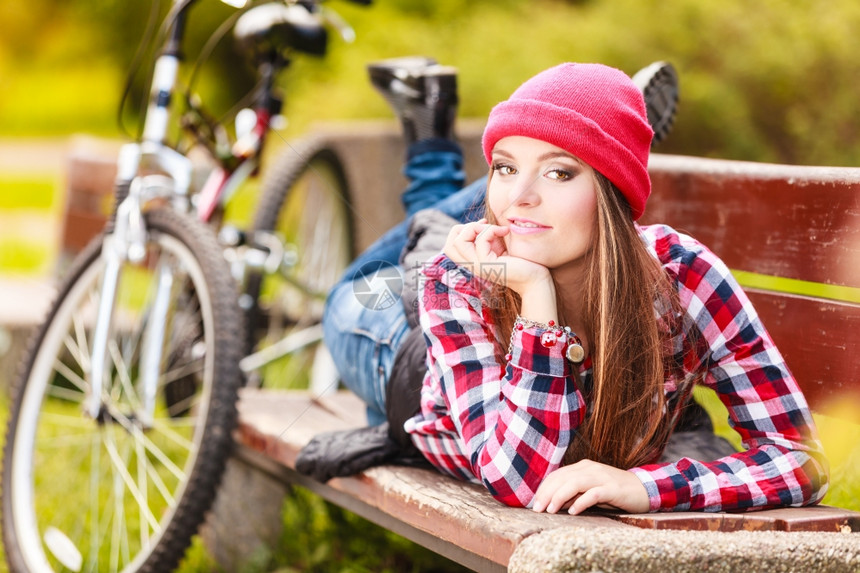 年轻女子骑着自行车在公园长凳上躺着休息图片