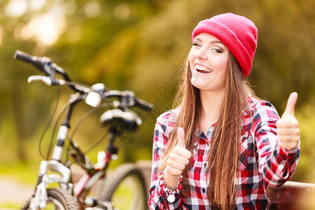 年轻女子骑着自行车在公园长凳上比划手势图片