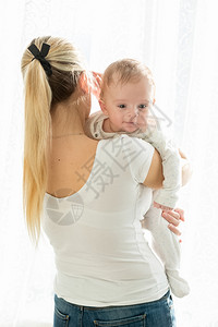 美丽的年轻女子肖像与她三个月大的男婴在窗户上女人高清图片素材