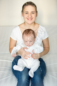 美丽的微笑女士坐在卧室里抱着可爱的宝在大腿上图片