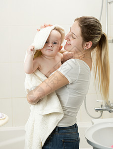 快乐的笑母亲肖像洗完澡后用毛巾擦婴儿的照顾高清图片素材