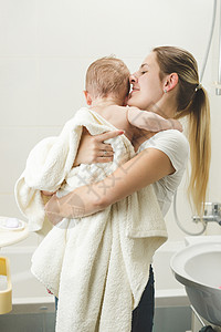 年轻母亲洗完澡后在浴室亲婴儿的肖像毛巾高清图片素材