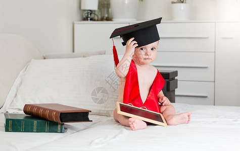 10个月大小男孩的有趣肖像身着毕业帽子的书图片