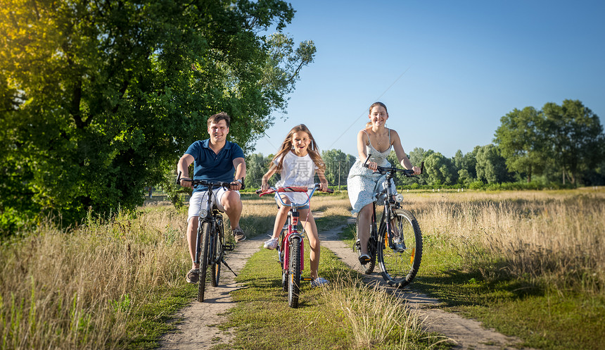 在草地骑自行车的年轻家庭快乐的年轻家庭图片
