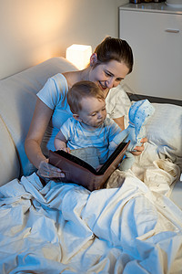美丽的笑母亲肖像读童话书给在床上的婴儿看图片