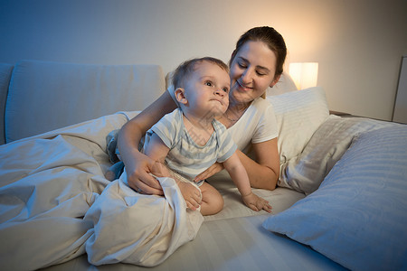 可爱的男婴和他母亲深夜上床睡觉的肖像背景