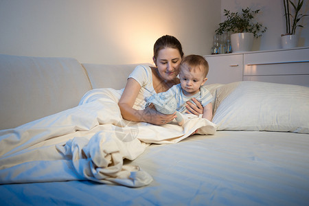 可爱的男孩和他母亲在睡觉前床上玩具图片