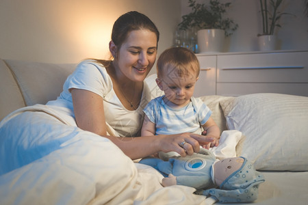 微笑的年轻母亲晚上和婴儿在床玩耍的肖像图片
