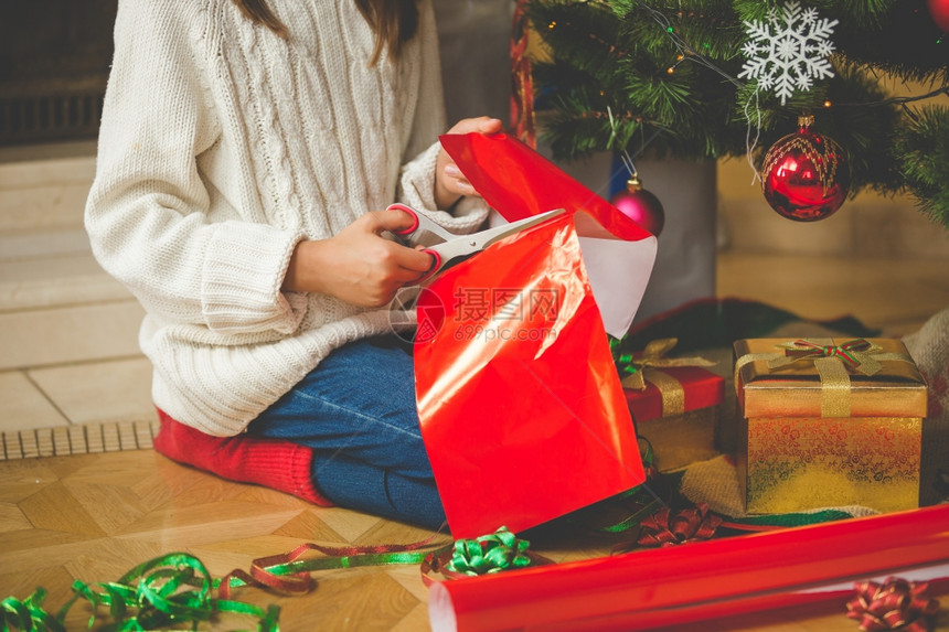 女孩坐在圣诞树下用剪刀红纸装饰礼物图片