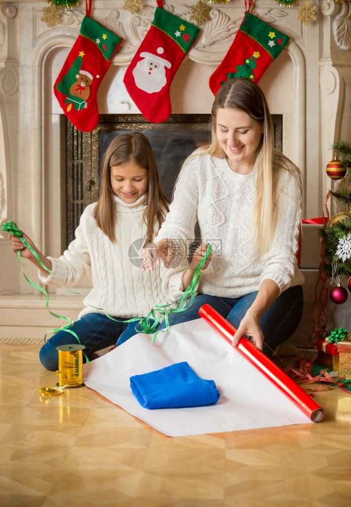 快乐的女儿和母亲在圣诞节前夕把毛衣包装在纸上图片