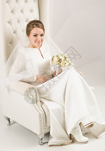 穿着长白色衣的优美新娘披着白皮臂椅图片