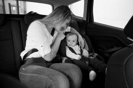 黑色和白的照片微笑母亲坐在汽车后座与婴儿一起坐在汽车后座上图片