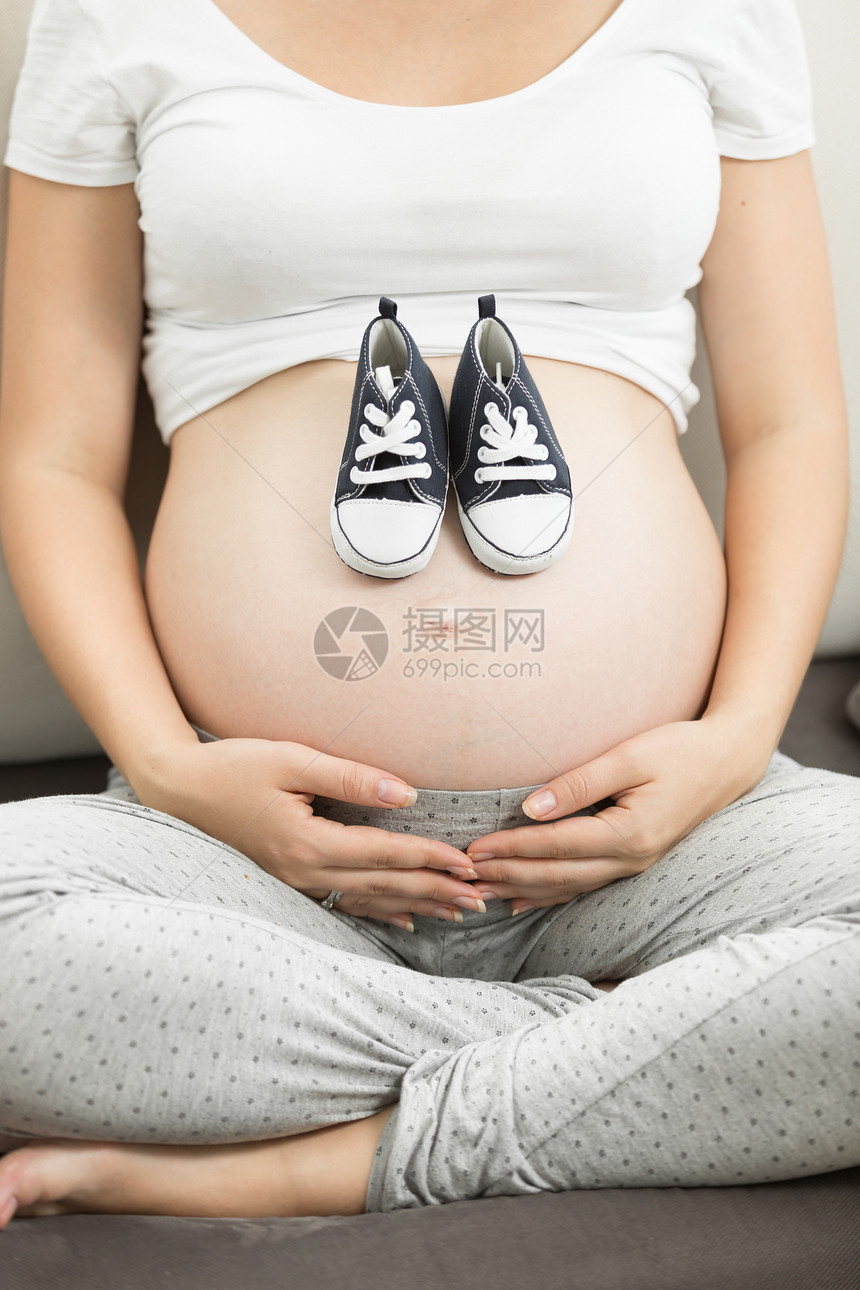孕妇将男婴的鞋子放在肚上的近视图像图片
