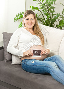坐在沙发上并进行超声波胎儿扫描的微笑孕妇图片