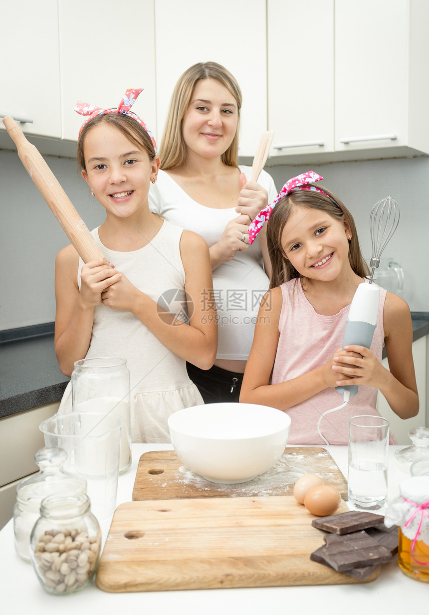 快乐的年轻母亲和两个女儿冒着厨房用具图片