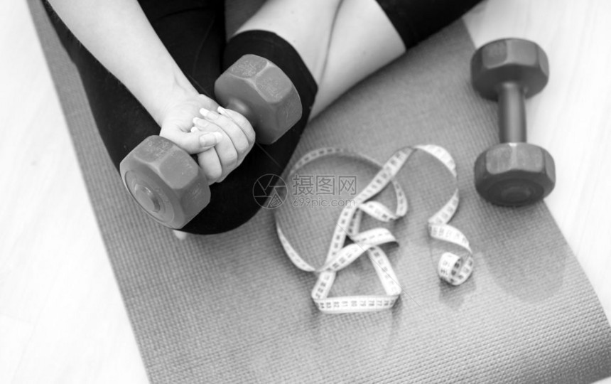 年轻女坐在健身垫子上举起哑铃的黑白照片图片