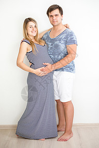 穿着脱光衣服披白墙的笑着怀孕夫妇图片