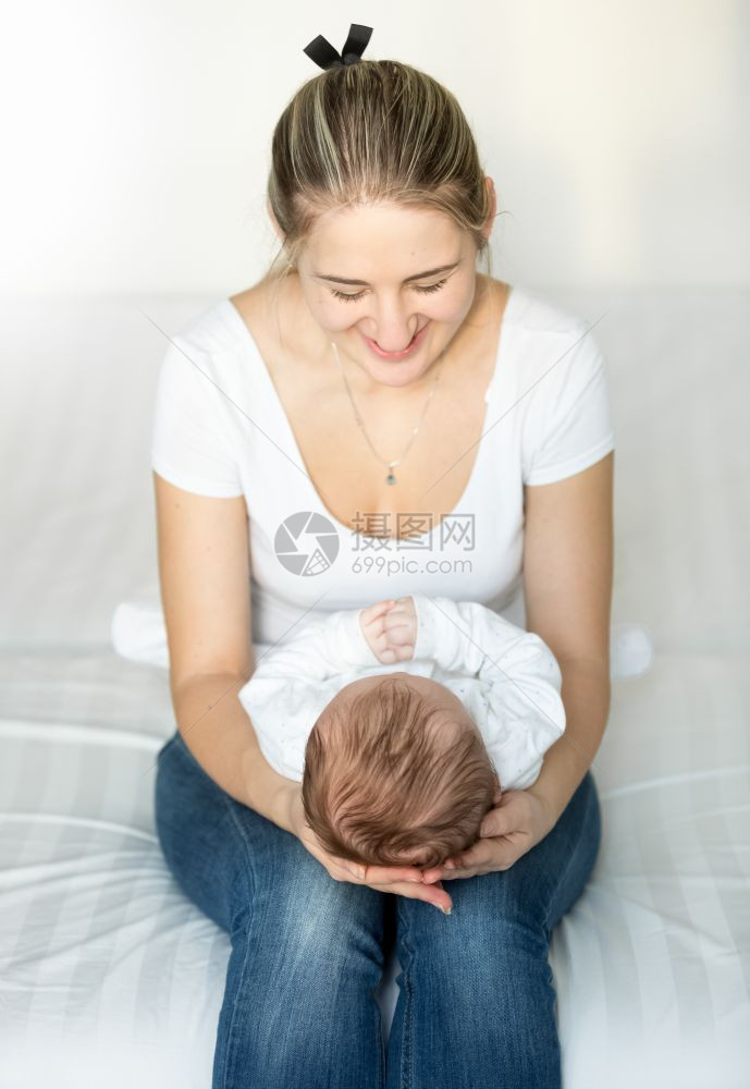 年轻母亲坐在床上将婴儿抓在手上图片
