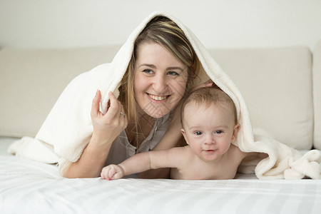 微笑的年轻母亲躺在床上带着白毯子的女婴儿躺在床上图片
