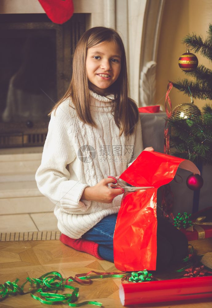 快乐的女孩坐在壁炉边包着圣诞礼物图片