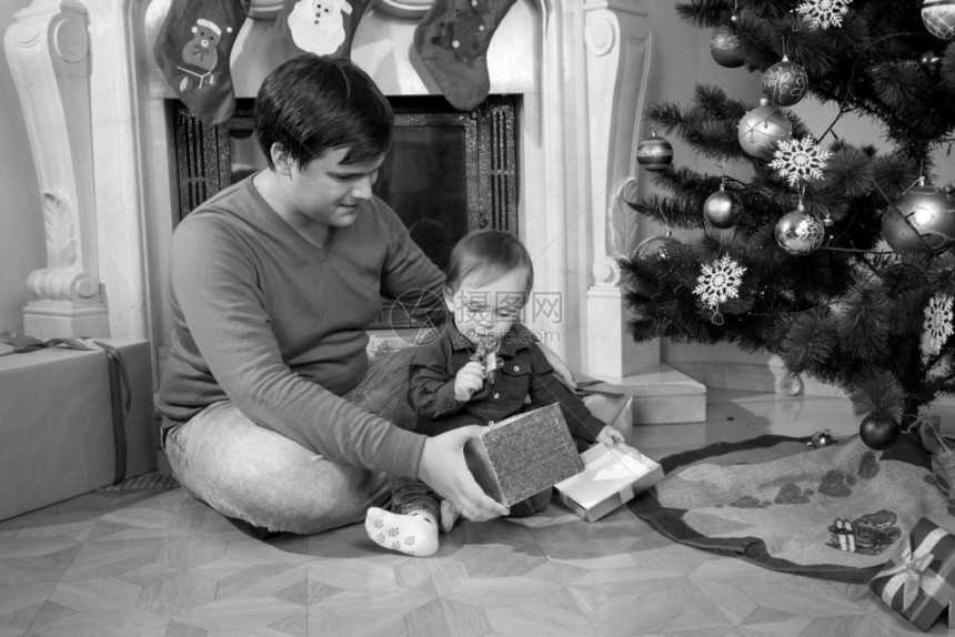 年轻父亲在圣诞树旁边玩儿一岁小男孩的黑白画面图片