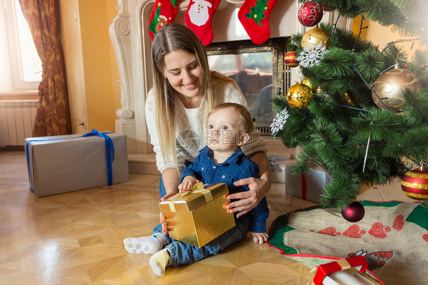 年轻母亲和她的儿女坐在圣诞树上看着礼物盒里图片