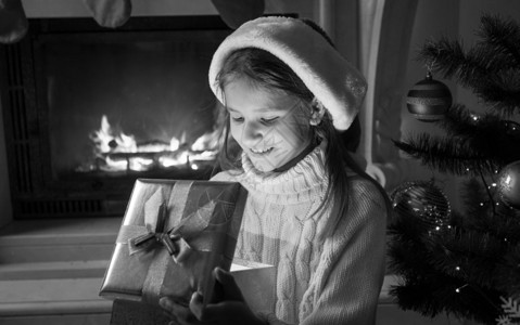 穿着圣诞老人帽子的可爱快乐女孩的黑白画像看着圣诞礼物盒里图片
