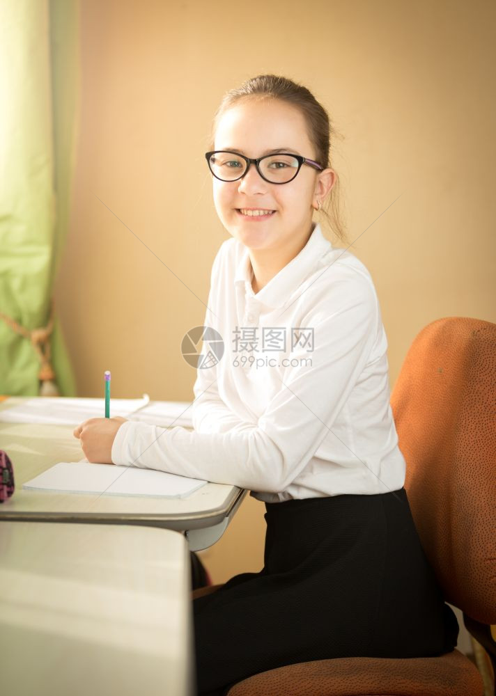 微笑着的女学生在课堂上坐桌后摆姿的肖像图片