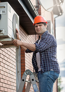 在建筑外墙上安装空调机的年轻工程师工具高清图片素材